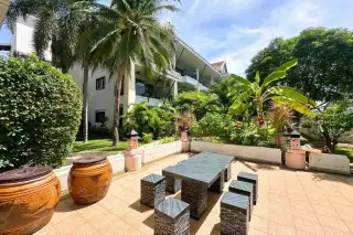 Sunrise Beach Residence outdoor patio with a dark grey table and stools, surrounded by tropical plants and palm trees.