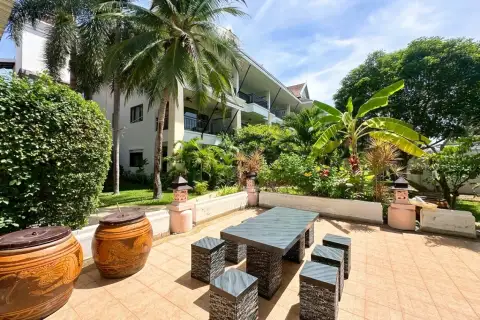 Sunrise Beach Residence outdoor patio with a dark grey table and stools, surrounded by tropical plants and palm trees.