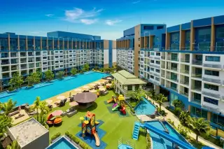 Laguna Beach Resort 2 large outdoor swimming pool surrounded by apartment buildings, palm trees, sun loungers, and green recreation areas.