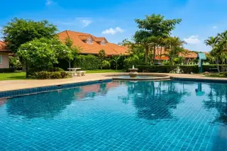Pattaya Hill Village 1 swimming pool with blue tiles, fountain, patio, and houses with orange roofs in background.