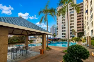 9 Karat Condo outdoor swimming pool with water slide, covered seating area, palm trees, and condo buildings under a blue sky.