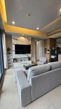 1 Bedroom Condo for Sale at Zire Wongamat living area with marble feature wall, mounted TV, and gray sofa