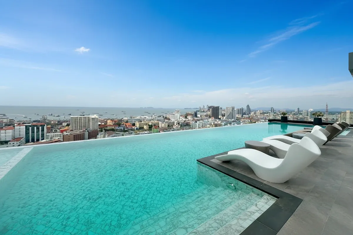 Arcadia Millennium Tower rooftop infinity pool with lounge chairs, offering expansive views of Pattaya city and the ocean.