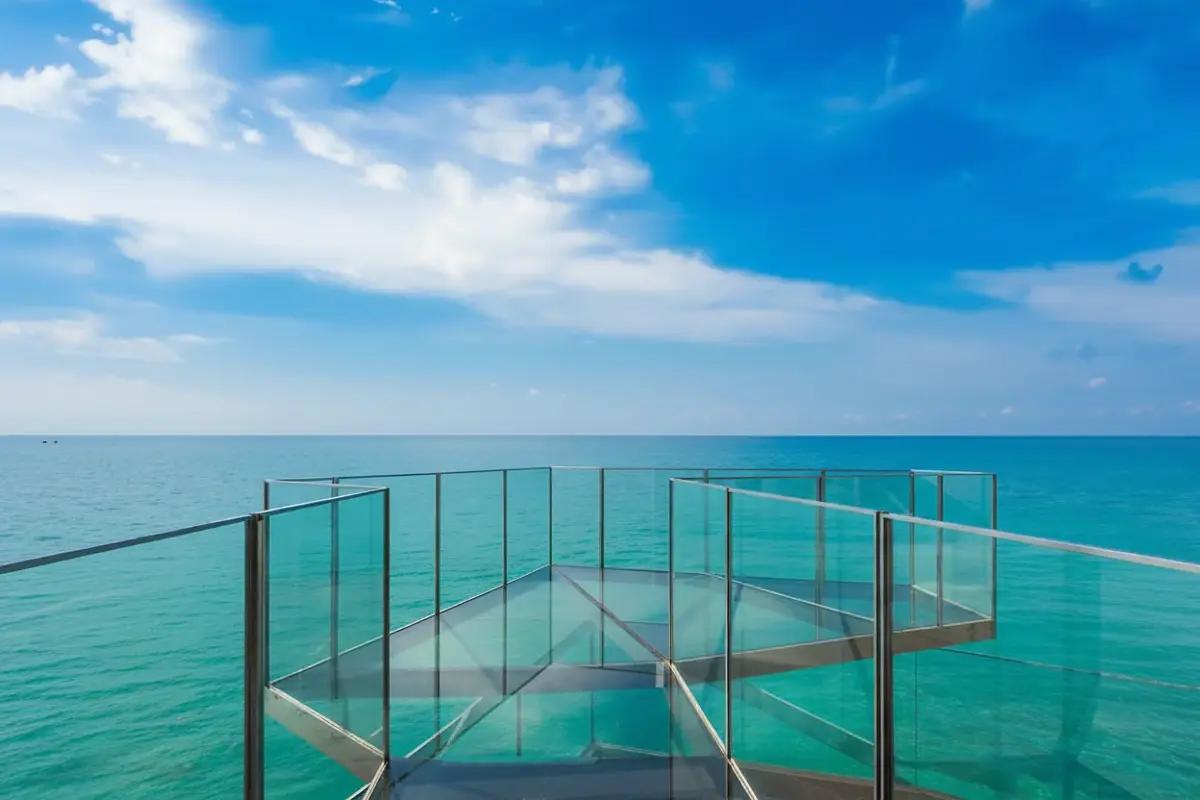 Arom Jomtien glass-bottomed skywalk extending over the ocean with a person in a hat.