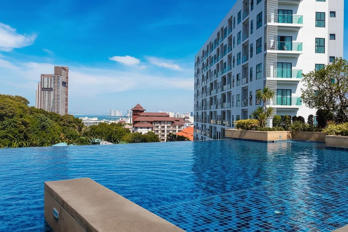 Axis Pattaya Condo rooftop infinity pool with a wooden deck and tropical plants, overlooking the city.