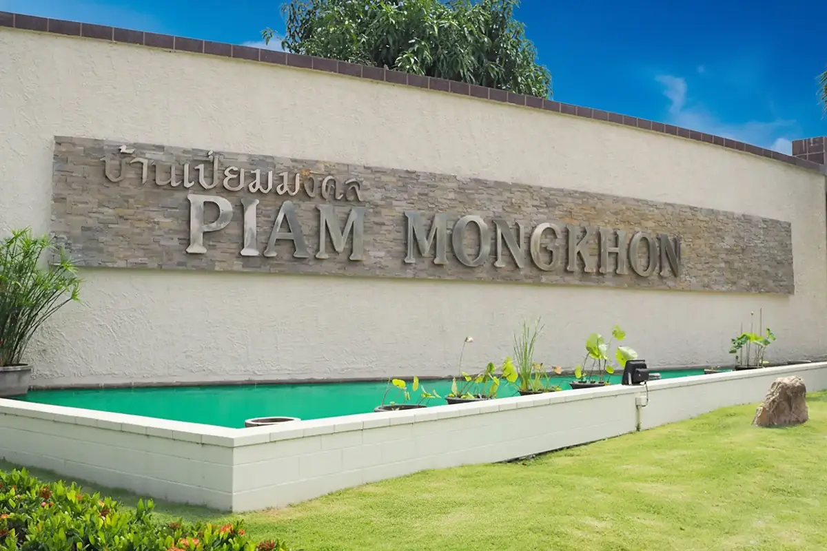 Baan Piam Mongkhon entrance sign with stone lettering, a small pond, and green landscaping.