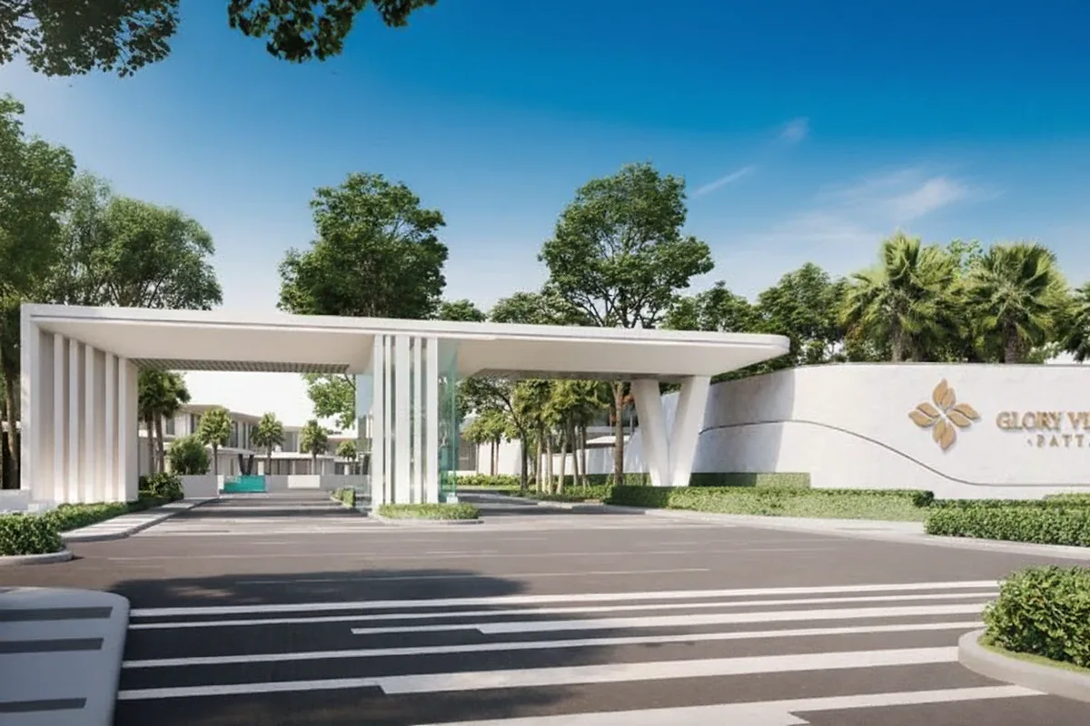 Glory Village Pattaya main entrance gate with modern design, white walls, and lush greenery.