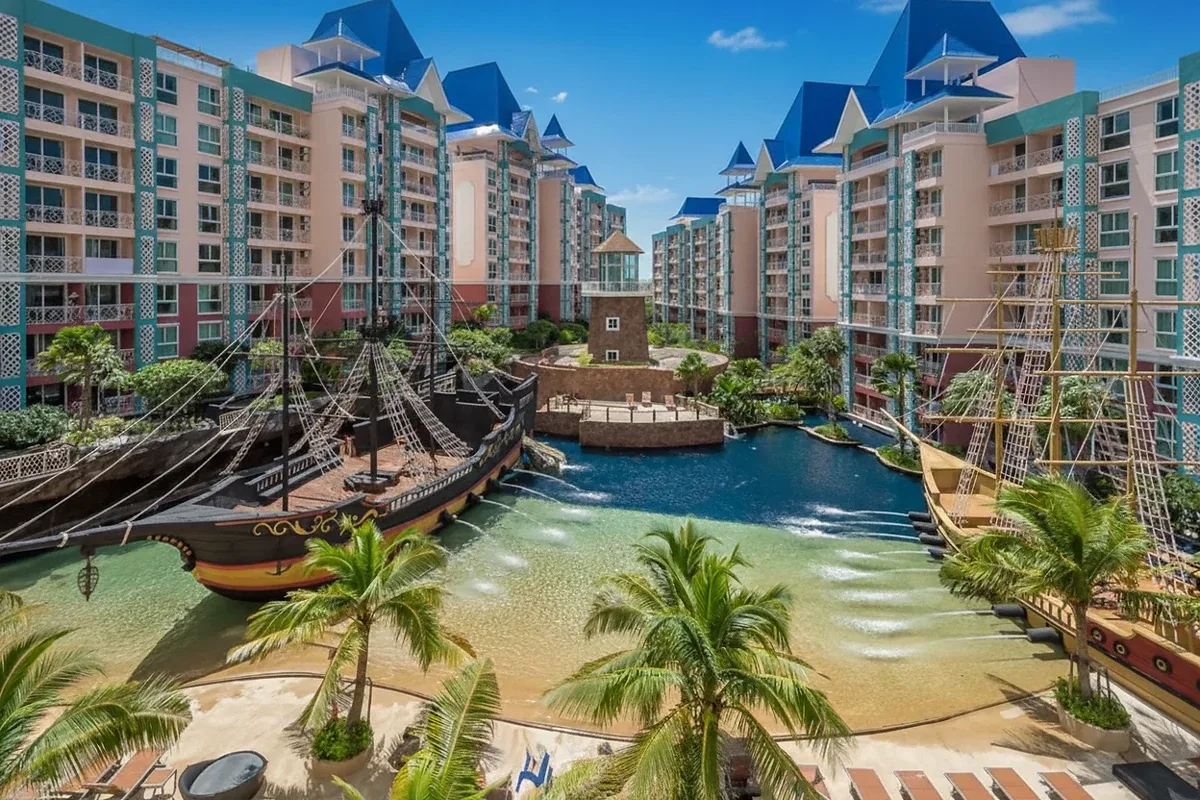 Grande Caribbean resort with pirate ships, sandy beach pool, and colorful buildings under a blue sky.