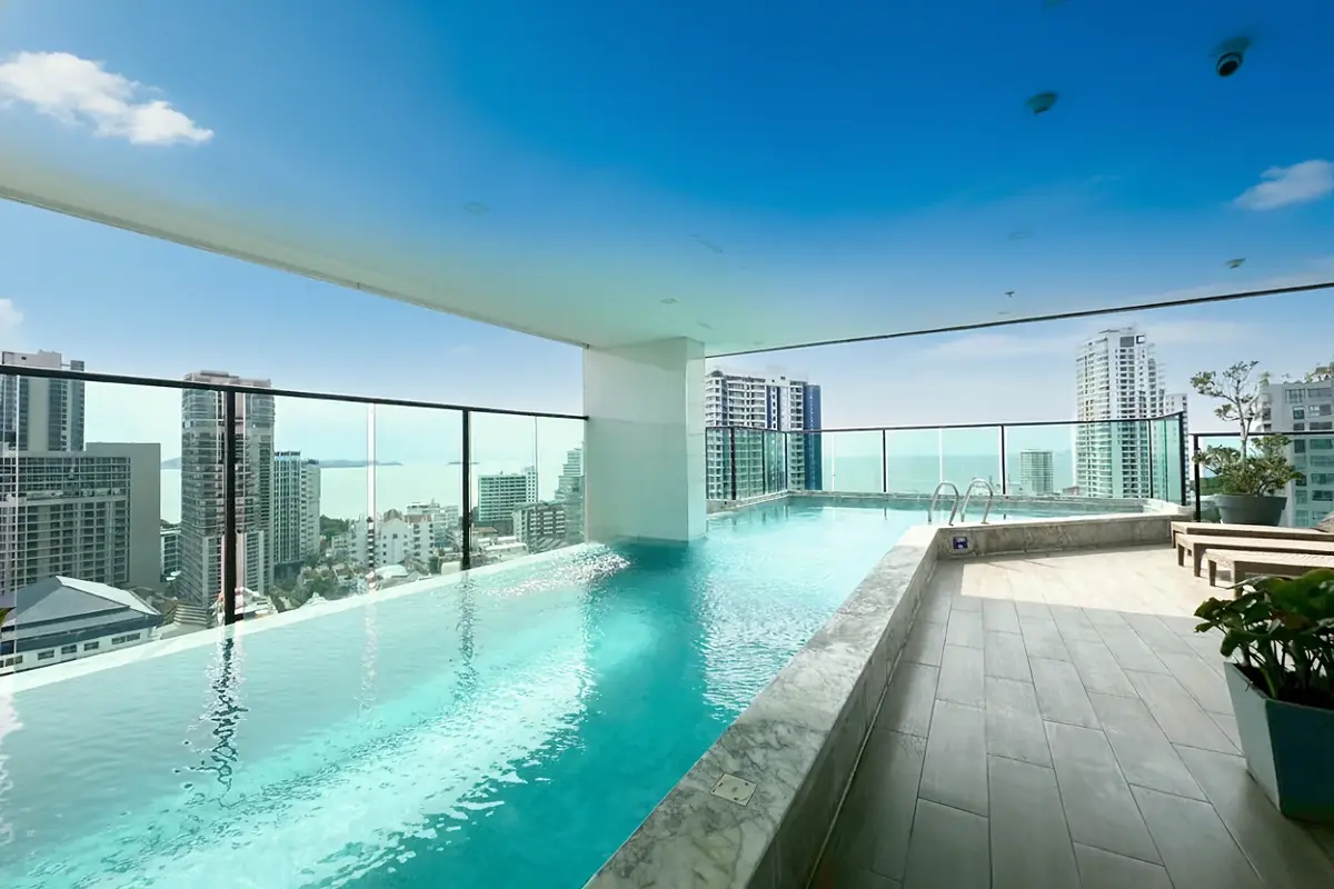 Jewel Pratumnak rooftop pool deck with lounge chairs, city, and ocean views.