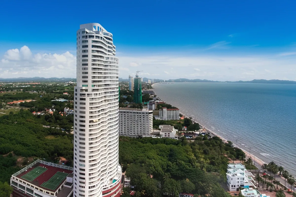 Metro Jomtien Condotel aerial view of the tall white building, coastline, and ocean under a blue sky.