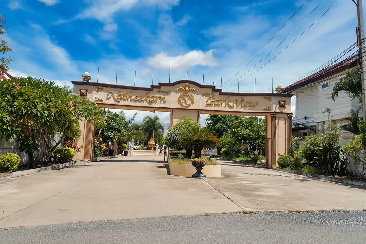 Natheekarn Park View main entrance gate with golden lettering and lush green landscaping under a blue sky.