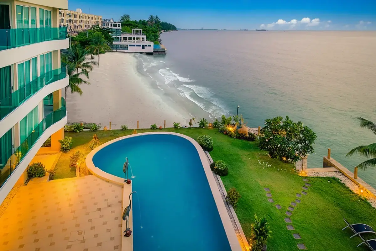 Paradise Ocean View: Aerial view of the pool, green lawn, sandy beach, and ocean with city skyline in distance.