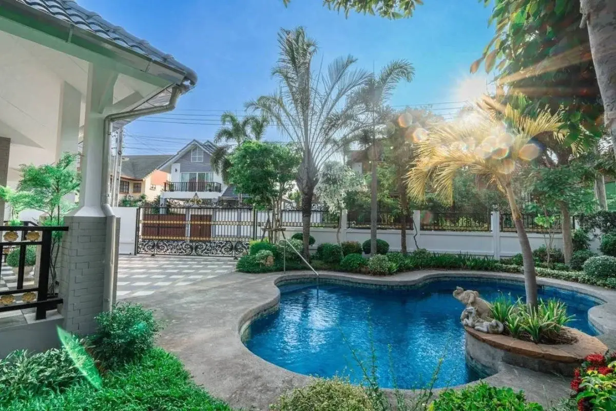 5 Bedroom House for Sale at Central Park 4. Sunny view of the house exterior, pool, and front gate with palm trees.