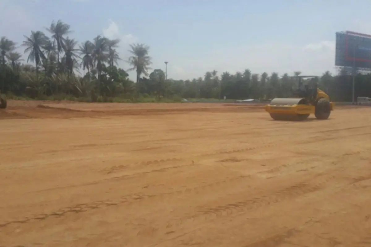 Land for Sale in Nong Pla Lai, large cleared dirt plot with a yellow road roller, palm trees, and a billboard.