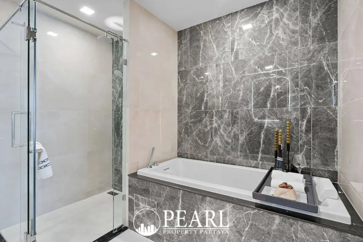 2 Bedroom Grand Executive Condo for Sale at Aquarous Jomtien Pattaya: Bathroom with bathtub, glass shower, and marble accent wall.