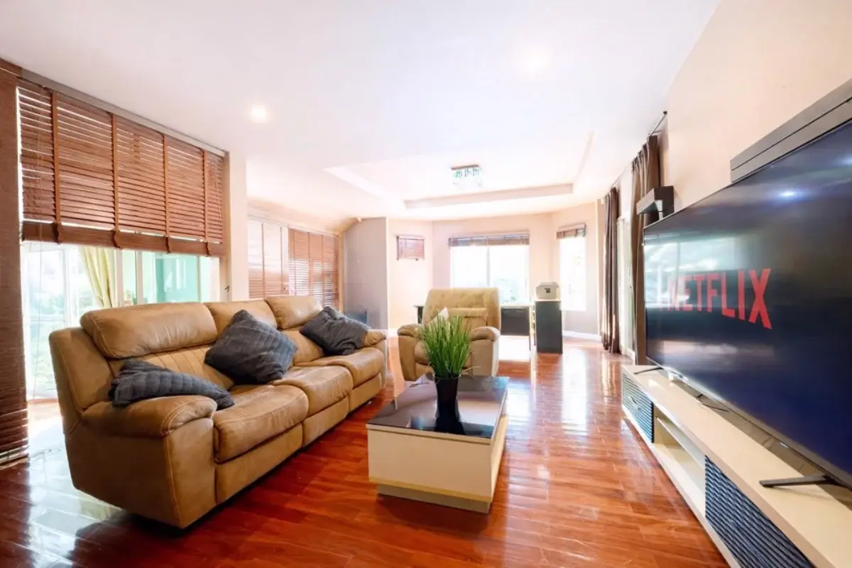 5 Bedroom House for Sale in Nong Prue, living room with brown leather sofa, wooden floor, and large TV.