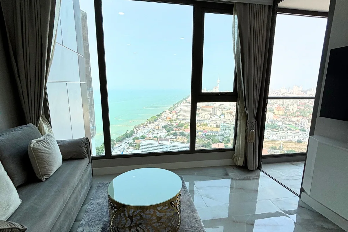 1 Bedroom Condo for Sale & Rent at Copacabana Beach Jomtien: Living room with sofa, coffee table, and panoramic ocean and city views.