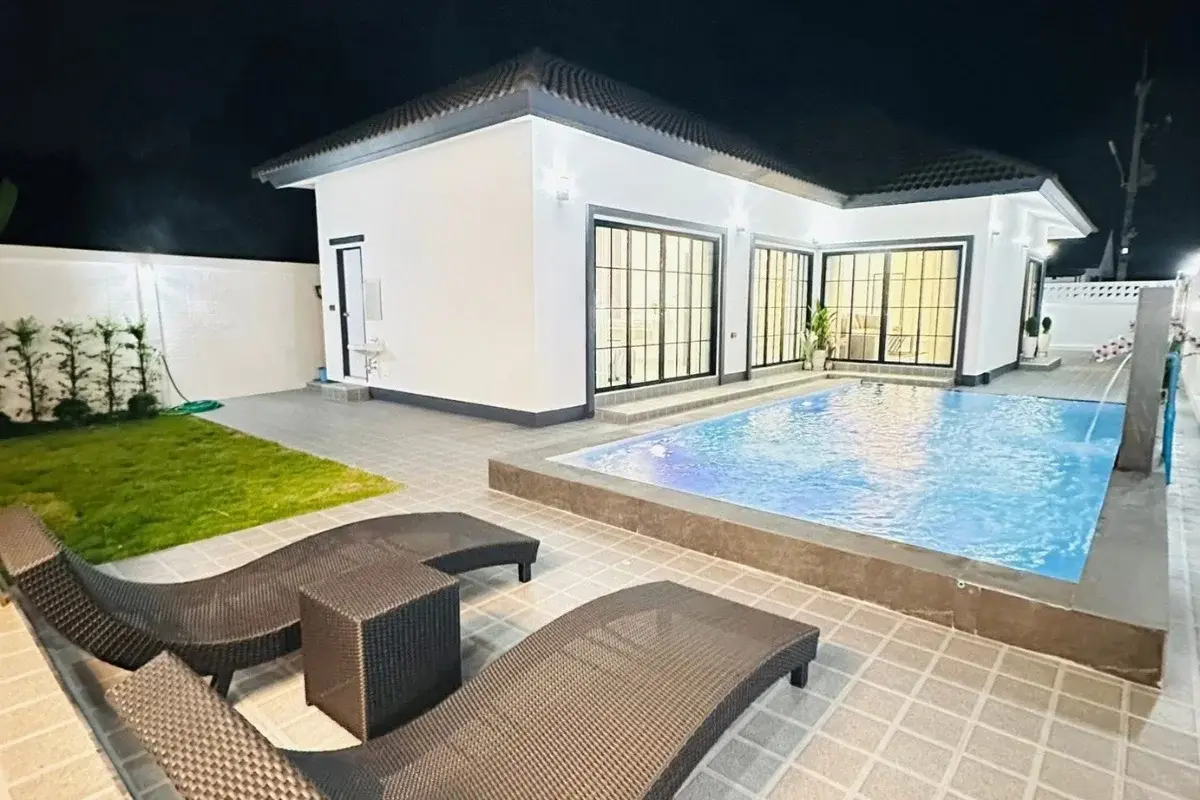 Rattanakorn Village 18 house at night with private swimming pool, two lounge chairs, and small grassy area.