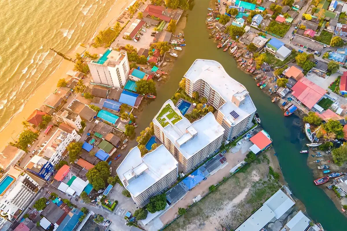 Whale Marina aerial top-down view showing buildings, pools, river with boats, and coastline.