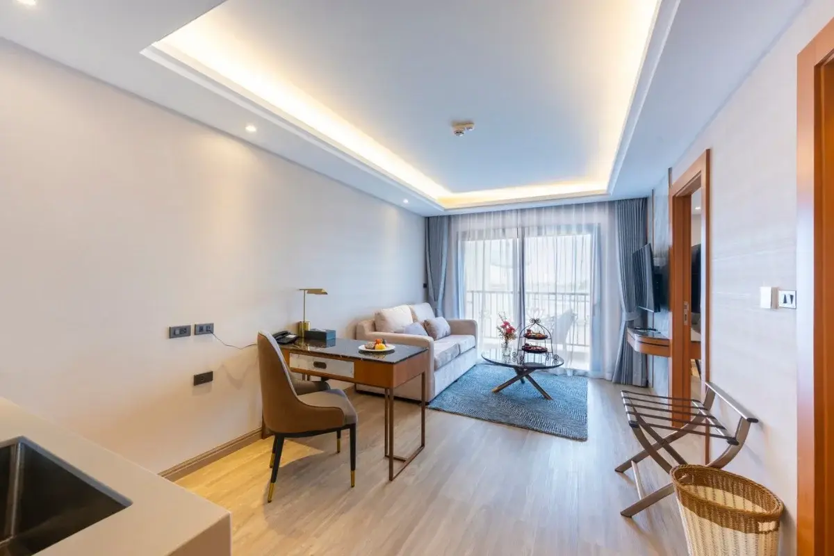 1 Bedroom Condo for Sale at Wyndham Jomtien Pattaya: Living room with sofa, desk, and balcony access through curtains.