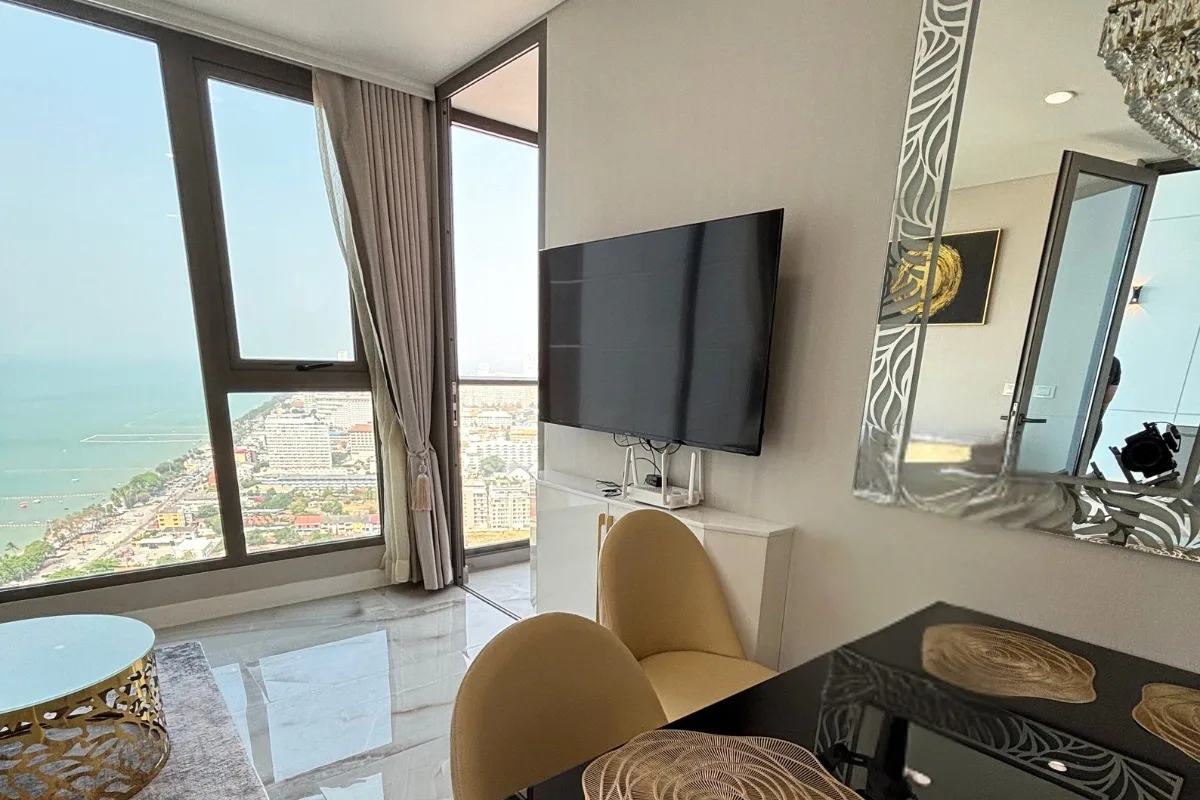 1 Bedroom Condo for Sale & Rent at Copacabana Beach Jomtien: Living area with wall-mounted TV, dining chairs, and city view.