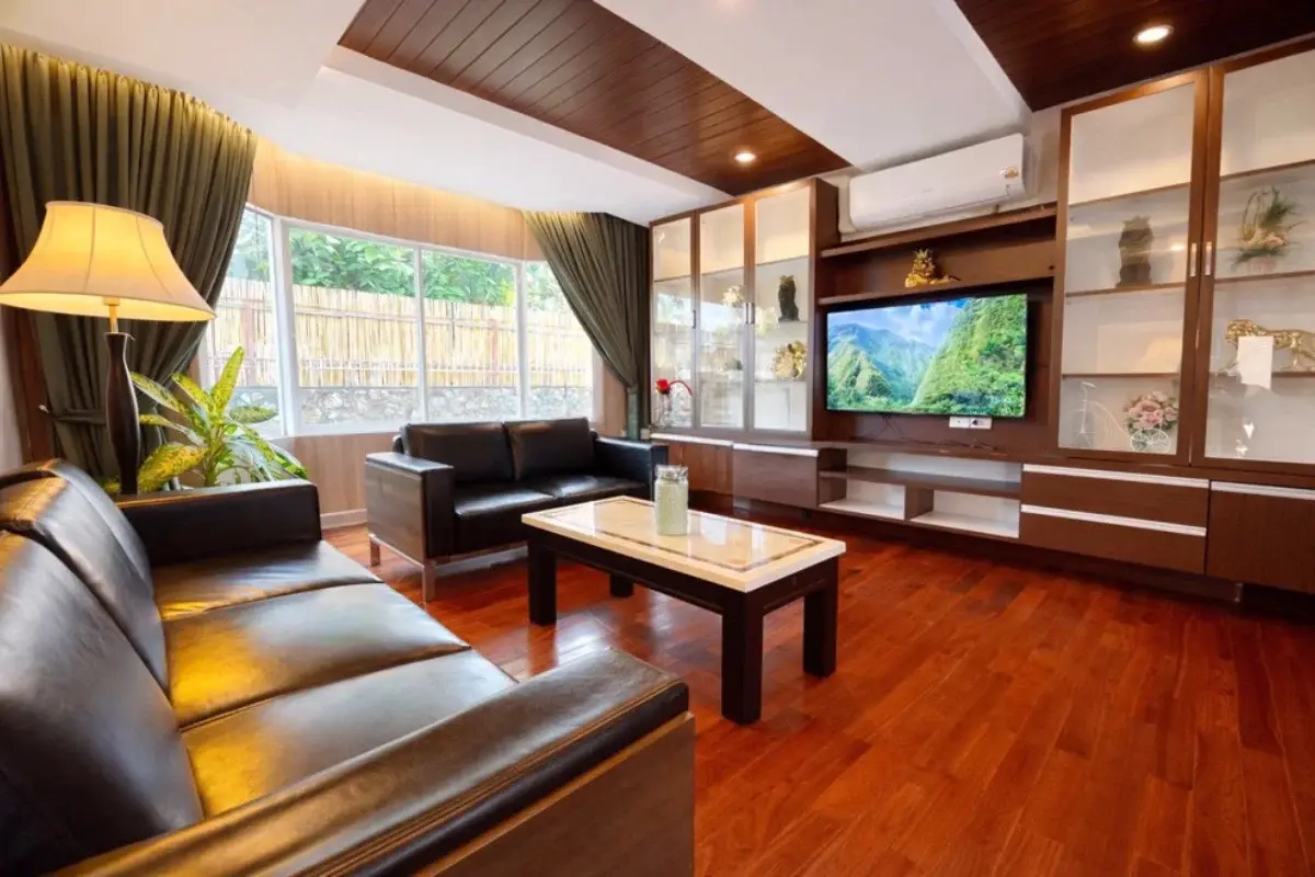 5 Bedroom House for Sale in Nong Prue, living room with black sofas, dark wood accents, and built-in display cabinets.