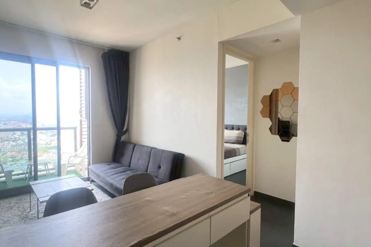 1 Bedroom Condo for Sale at Unixx South Pattaya: living area with sofa, large window, and partial view of the bedroom entrance.