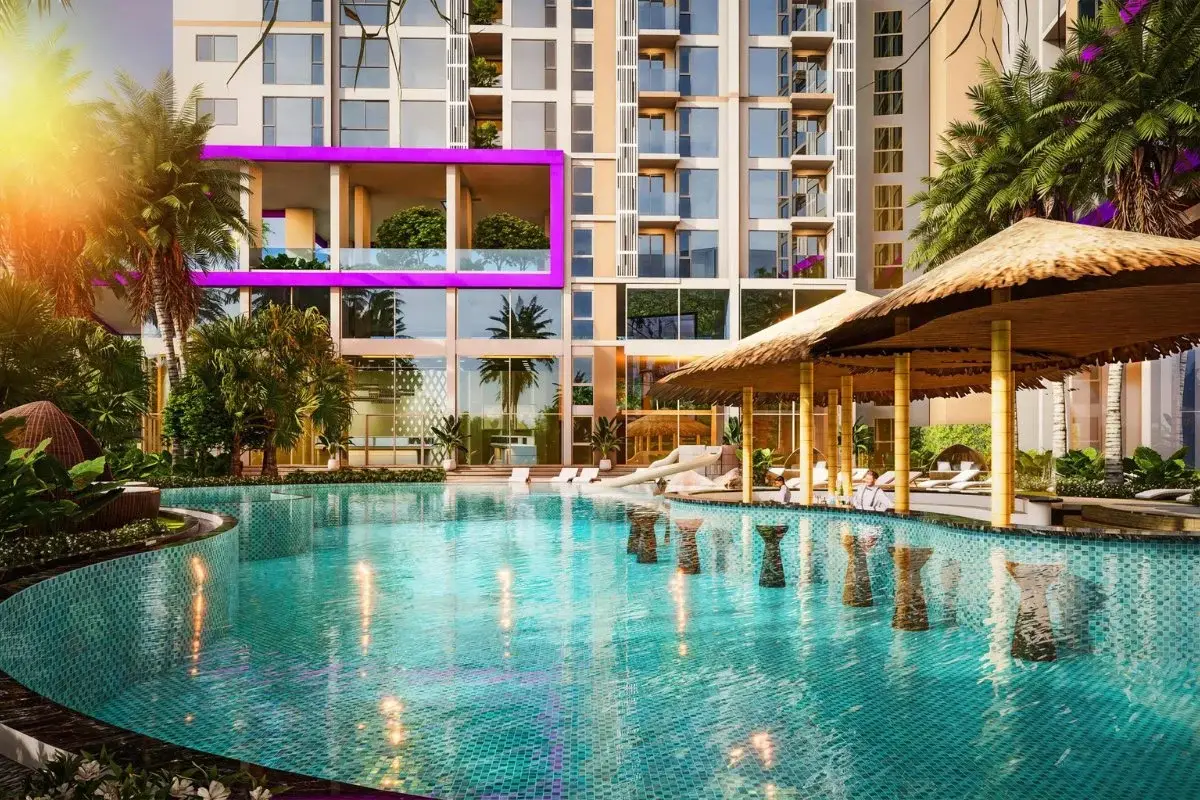 The Riviera Santa Monica turquoise swimming pool with straw umbrellas, surrounded by tropical plants and the building.