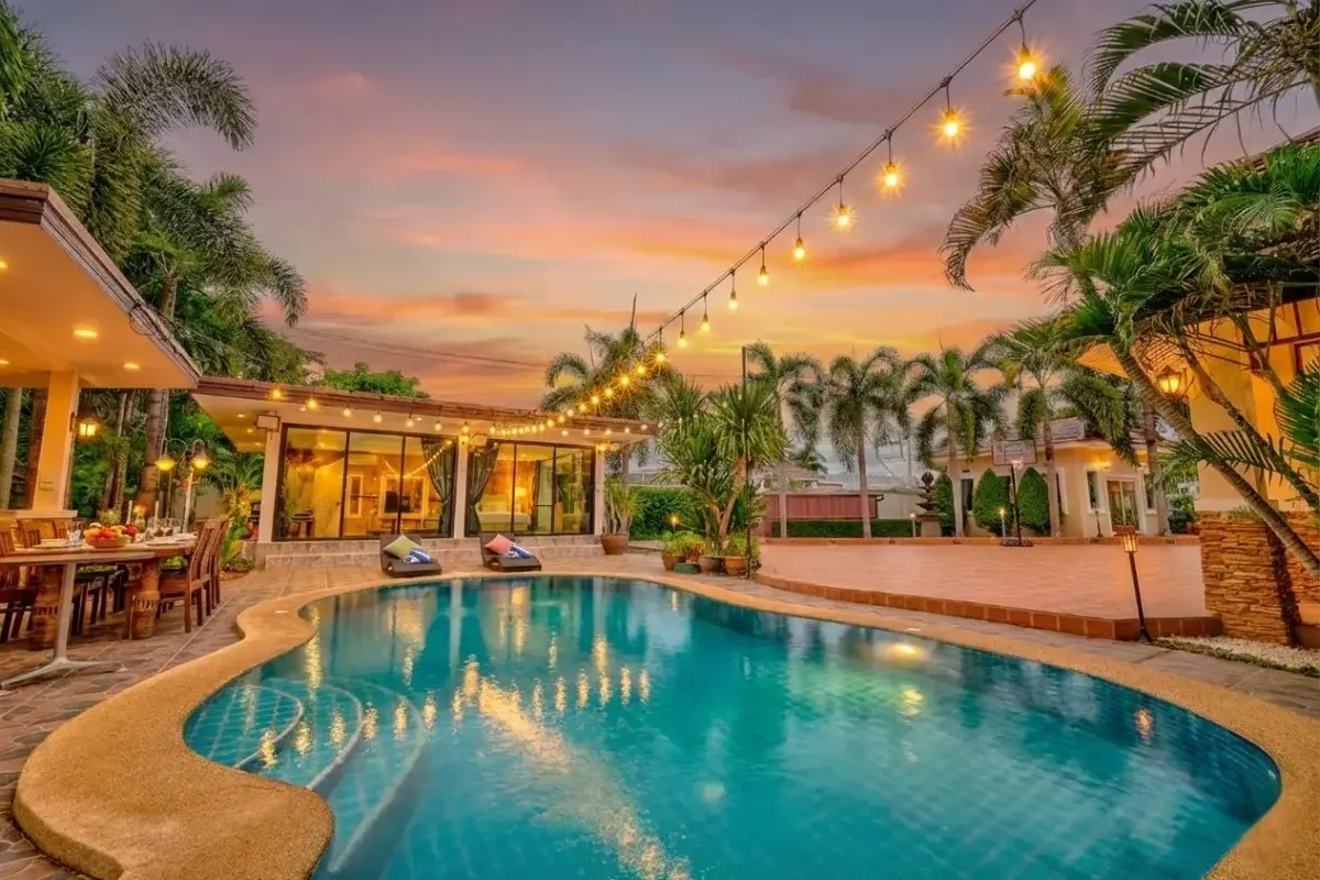 5 Bedroom House for Sale in Nong Prue, swimming pool area at sunset with string lights and lush palm trees.