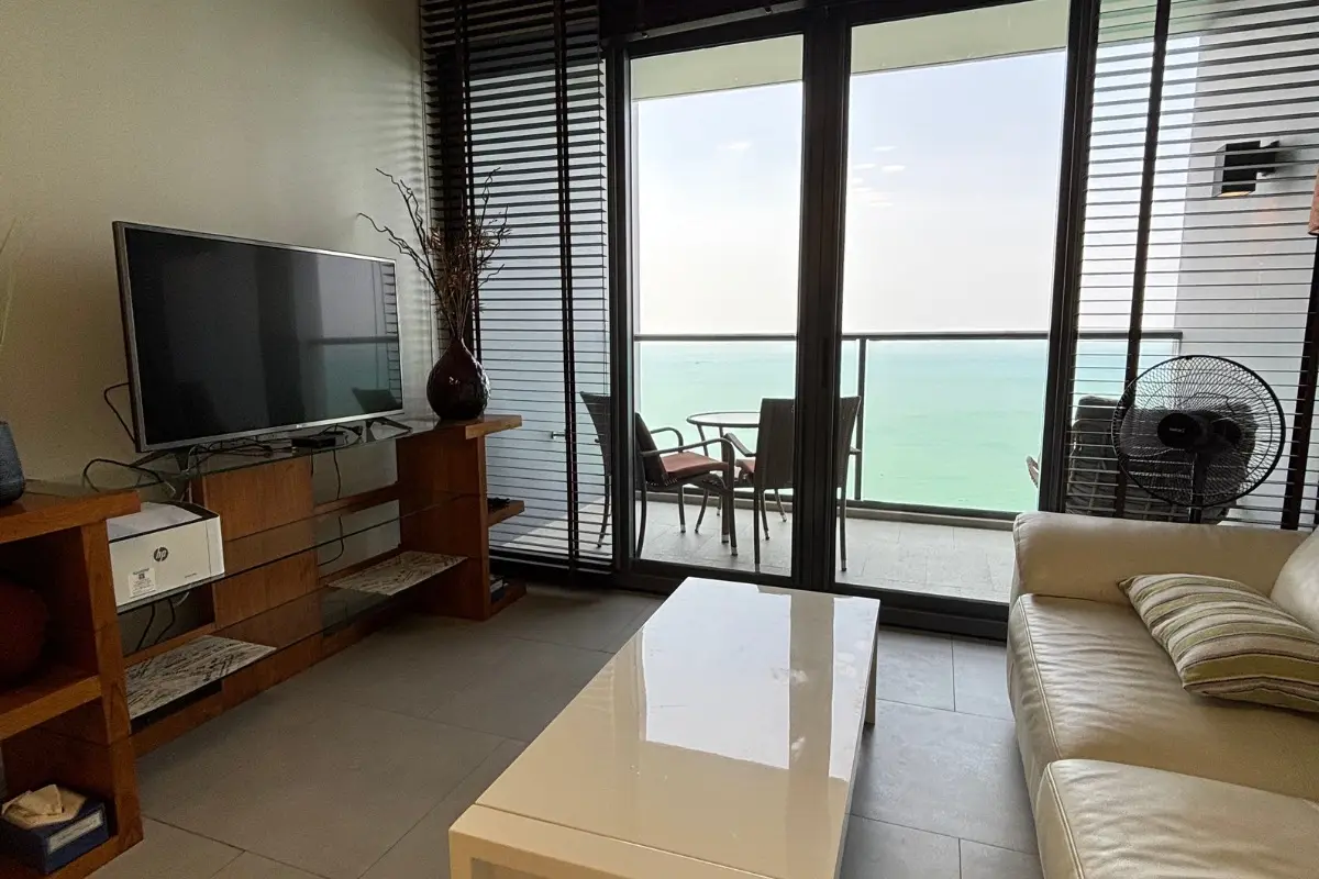1 Bedroom Condo for Sale at Zire Wongamat living room with TV, sofa, and balcony with ocean view.