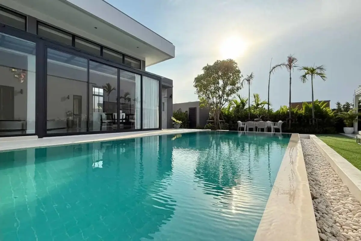 3 Bedroom House for Sale & Rent at The Prospect: Long swimming pool reflecting the sun, with a modern house exterior and palm trees.