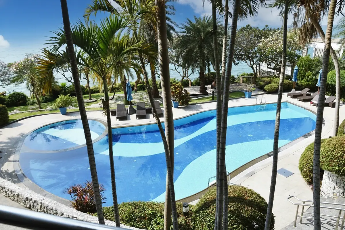 Sugar Beach resort pool with lounge chairs, surrounded by palm trees and ocean in the background.