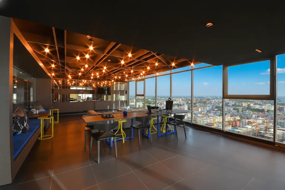 The Base Central Pattaya rooftop infinity pool with people swimming and city-ocean views.