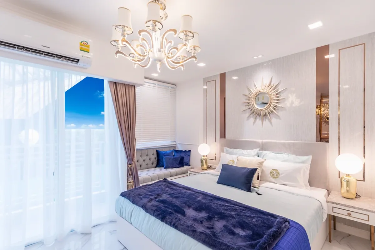 The Empire Tower Pattaya, a luxurious bedroom with a large bed, elegant chandelier, sunburst mirror, and balcony access.
