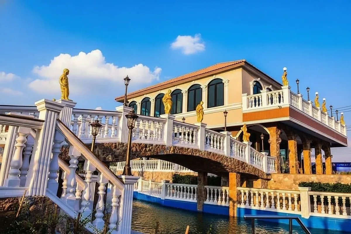 The Lake Huay Yai ornate clubhouse building with a decorative bridge over a water feature under a clear sky.