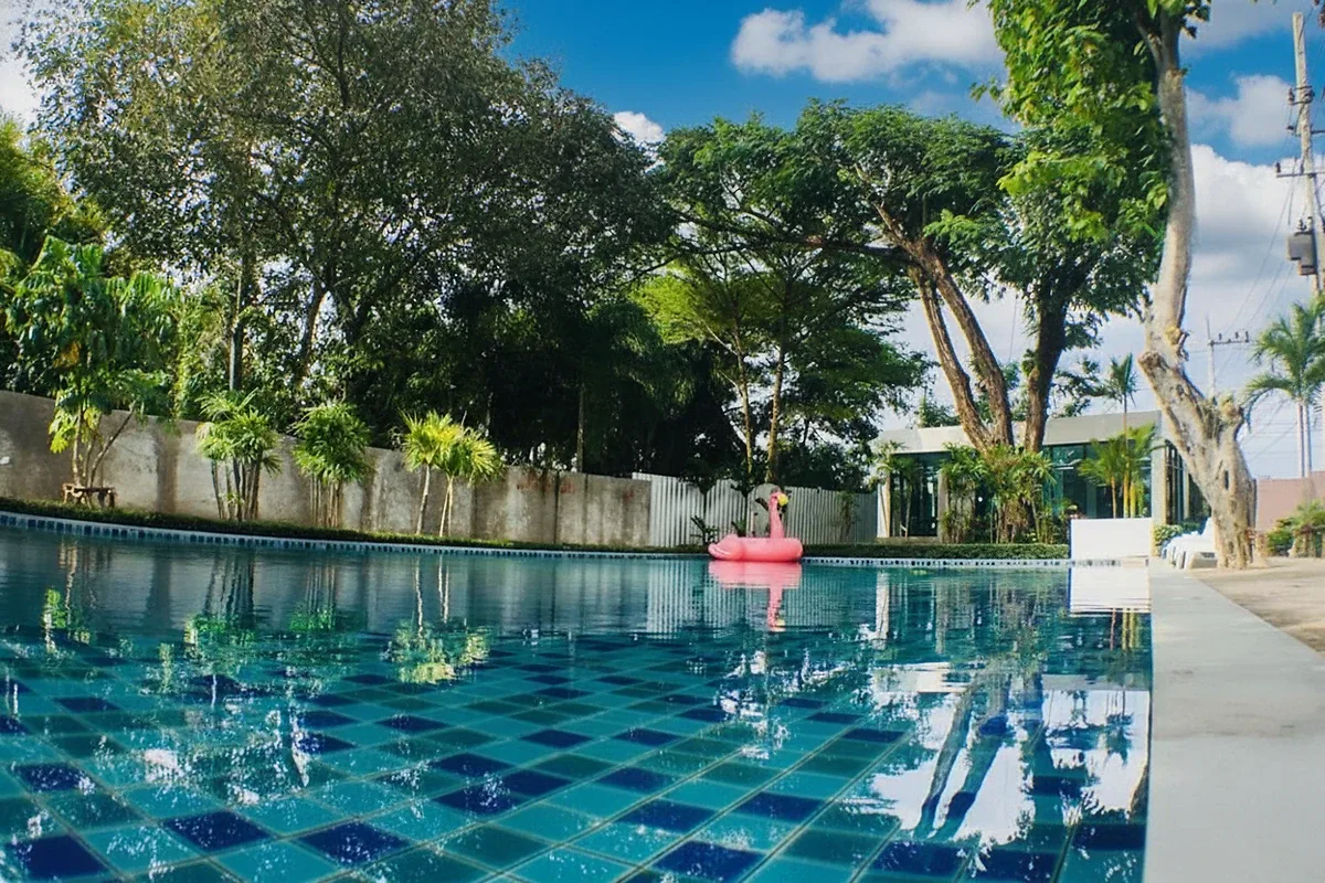 The Maple Pattaya outdoor swimming pool with a wooden swing structure and palm trees.