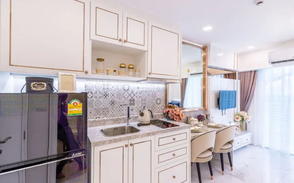 The Empire Tower Pattaya, a modern, compact kitchen with white cabinets, a small refrigerator, and a dining nook.