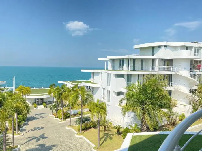 Pure Sunset Beach modern white condo complex with palm trees, ocean view, and a paved driveway under a blue sky.