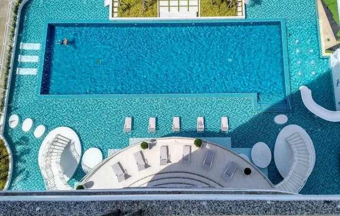 The Residences @ Dream Pattaya outdoor swimming pool with blue tiles, lounge chairs, and a white spiral staircase.