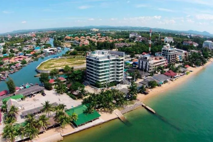 Water's edge aerial view of a modern condo building, sandy beach, river, and town in Pattaya, Thailand.