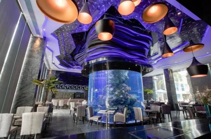 Centara Avenue Residence and Suites restaurant interior with a large cylindrical aquarium and purple ambient lighting at night.