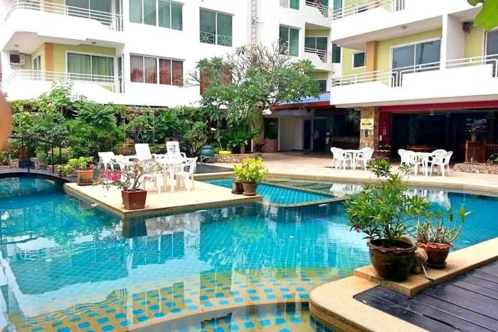 Jada Beach: Outdoor swimming pool with blue tiles, small seating islands, lush greenery, and the condo building in the background.