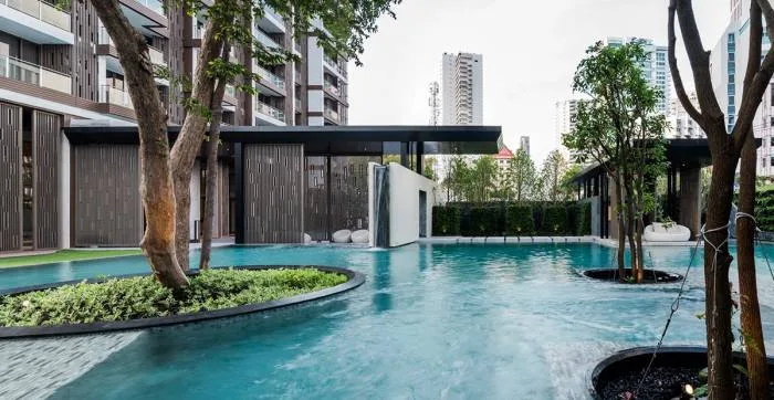 Baan Plai Haad beach area with white sand, lounge chairs, large green trees, and condo building in background.