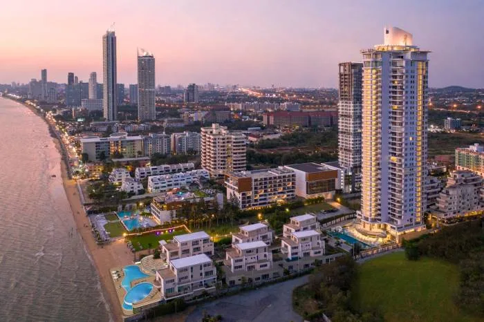 The Residences @ Dream Pattaya aerial view of the illuminated high-rise building and Pattaya coastline at dusk.