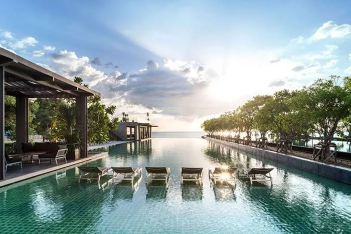 Reflection Jomtien Beach: Modern high-rise building exterior with illuminated pool, lounge chairs, and waterfall features at dusk.