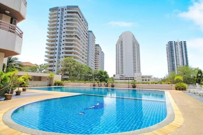 Kieng Talay outdoor swimming pool with surrounding greenery and tall residential buildings under a blue sky.