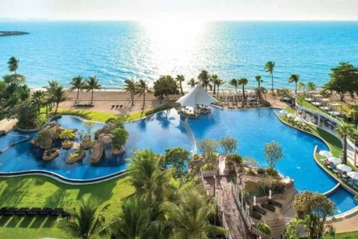 Movenpick Residences large resort pool with a swim-up bar, surrounded by palm trees, lush gardens, and a beach leading to the ocean.