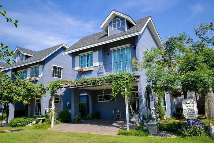 Winston Village light blue house with covered patio, climbing vines, dormer windows, and green lawn.
