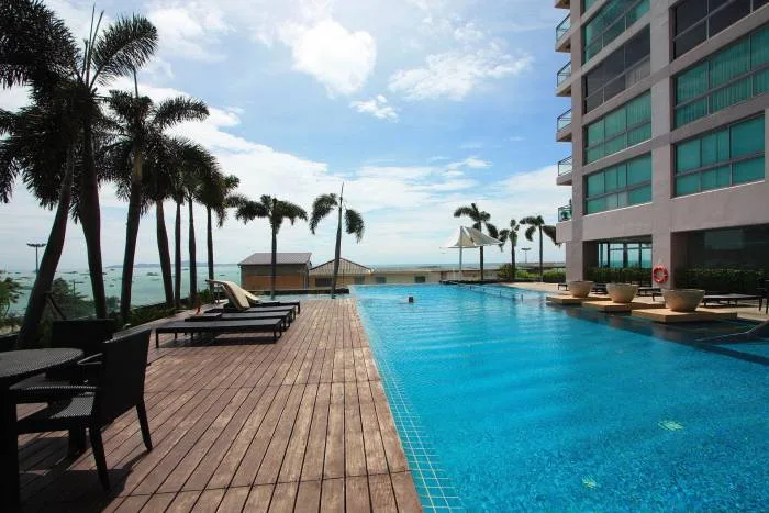 Northshore Pattaya outdoor swimming pool with ocean view, wooden deck, and palm trees under a blue sky.