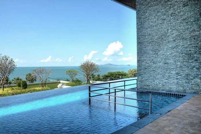Cetus Beachfront infinity pool with ocean view and a stone wall under a clear blue sky.